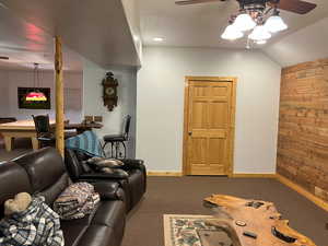 Carpeted living room featuring wood walls, ceiling fan, baseboards, and lofted ceiling