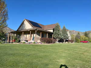 Farmhouse-style home with roof mounted solar panels, a front lawn, a mountain view, and covered porch