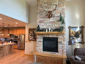 Living room featuring light wood-type flooring, a stone fireplace, recessed lighting, and baseboards