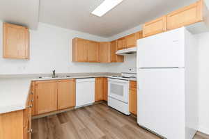 Kitchen featuring white appliances, under cabinet range hood, light brown cabinetry, light wood-style floors, and a sink
