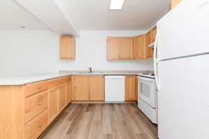 Kitchen with white appliances, light wood-style flooring, a sink, light brown cabinetry, and light countertops