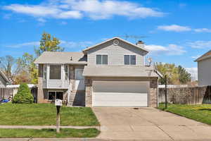 Split level home featuring brick siding, an attached garage, concrete driveway, and a chimney
