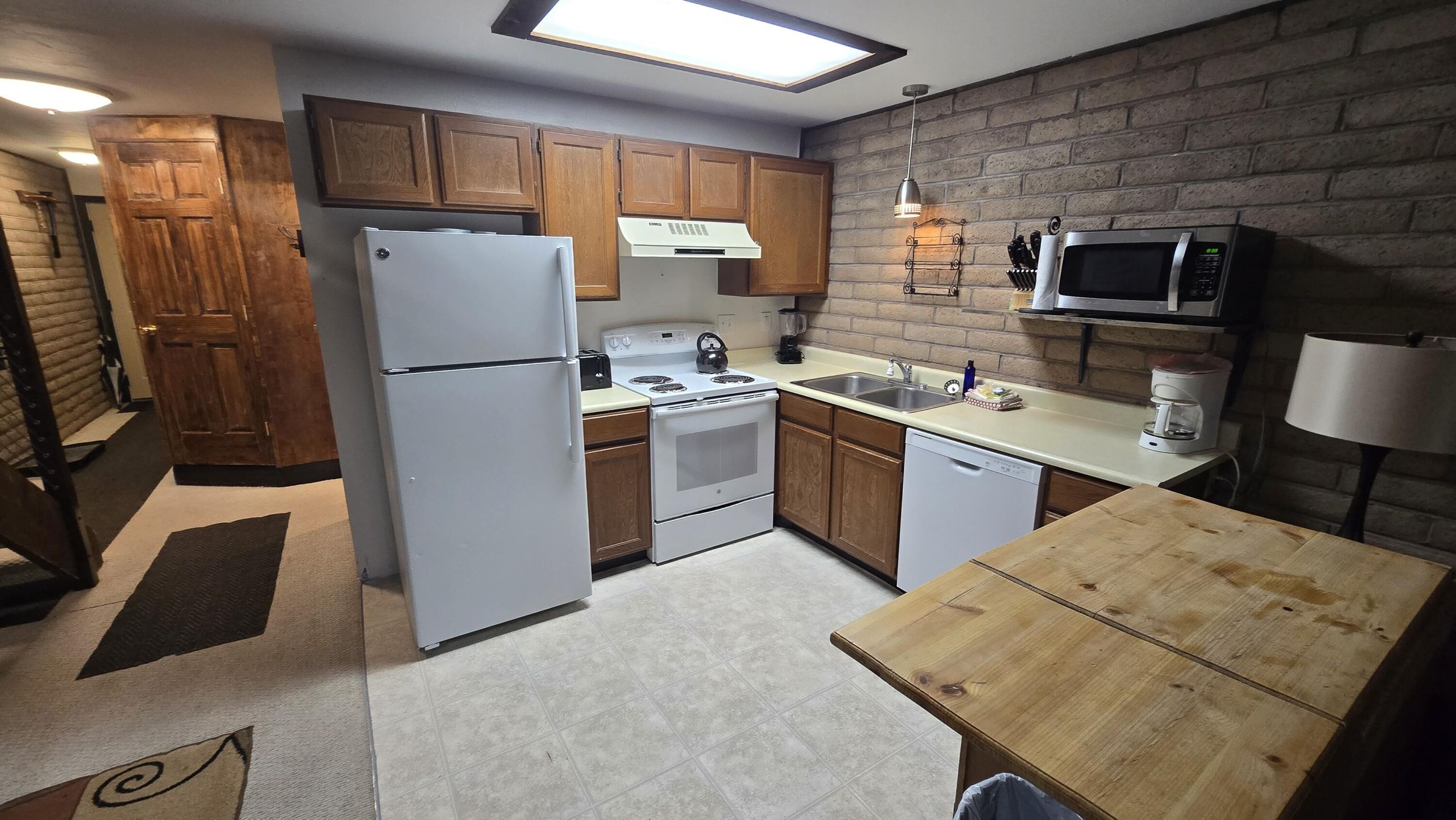 Kitchen with white appliances, a sink, brick wall, under cabinet range hood, and hanging light fixtures