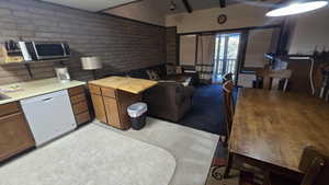 Kitchen featuring dishwasher, stainless steel microwave, brown cabinetry, brick wall, and butcher block counters