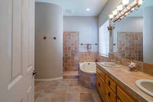 Bathroom featuring a whirlpool tub, double vanity, tile patterned flooring, walk in shower, and baseboards