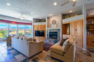 Living area with ceiling fan, a textured ceiling, a tiled fireplace, recessed lighting, and stone finish flooring