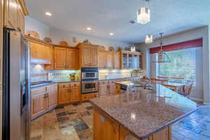 Kitchen with stainless steel appliances, a sink, a textured ceiling, an island with sink, and decorative backsplash