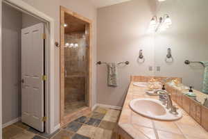 Full bathroom featuring a stall shower, baseboards, double vanity, and stone tile flooring