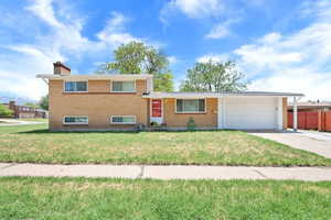 Tri-level home featuring an attached garage, brick siding, driveway, and a chimney