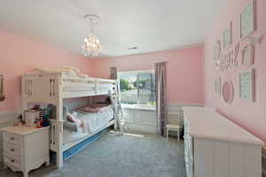 Carpeted bedroom with a wainscoted wall, a chandelier, and a decorative wall