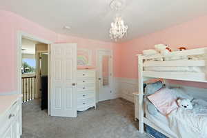 Bedroom with light colored carpet, a chandelier, and wainscoting