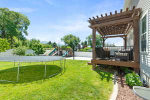 View of yard featuring a pergola, a playground, a trampoline, and a deck with mountain view