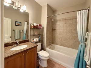 Bathroom with toilet, shower / bathtub combination with curtain, vanity, and wood finished floors