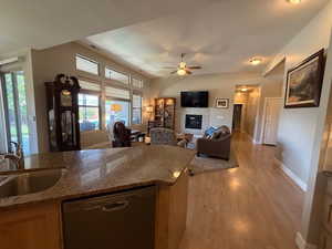 Kitchen with dishwashing machine, a sink, light wood finished floors, ceiling fan, and a glass covered fireplace