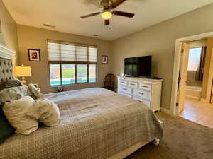 Bedroom featuring light carpet, baseboards, light tile patterned floors, ensuite bathroom, and ceiling fan
