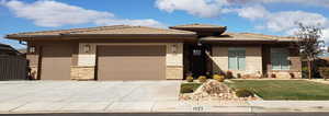 Prairie-style house with an attached garage, stone siding, concrete driveway, a front yard, and a tiled roof