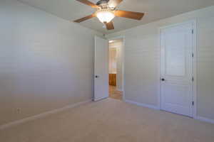Unfurnished bedroom with light colored carpet, baseboards, and a ceiling fan