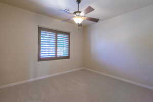 Empty room with light colored carpet, baseboards, and a ceiling fan