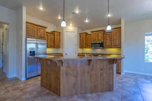 Kitchen with appliances with stainless steel finishes, brown cabinets, baseboards, a kitchen breakfast bar, and recessed lighting