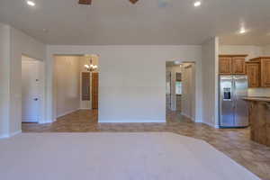 Kitchen with stainless steel fridge, a chandelier, baseboards, a ceiling fan, and brown cabinetry