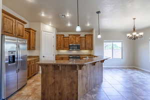 Kitchen featuring appliances with stainless steel finishes, brown cabinets, a breakfast bar, pendant lighting, and a chandelier