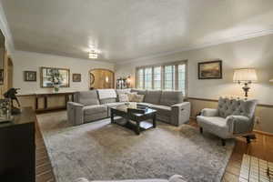 Living room featuring arched walkways, ornamental molding, baseboards, tile patterned floors, and a textured ceiling