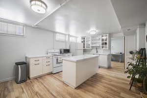 Kitchen featuring white appliances, a sink, white cabinets, a center island, and light wood-style flooring