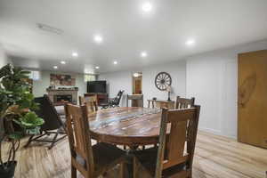 Dining room with a lit fireplace, light wood-style floors, and recessed lighting