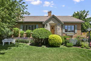 View of front of home with a front yard, a chimney, brick siding, and stone siding