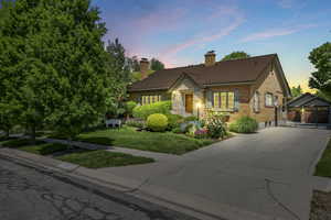 View of front of property featuring driveway, a chimney, brick siding, and a yard
