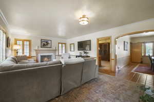 Living room featuring arched walkways, tile patterned flooring, ornamental molding, and a brick fireplace