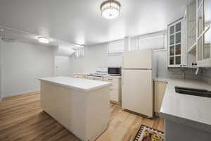 Kitchen with white appliances, a kitchen island, light countertops, glass insert cabinets, and light wood-type flooring