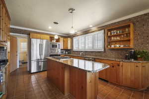 Kitchen featuring appliances with stainless steel finishes, a sink, plenty of natural light, tasteful backsplash, and ornamental molding