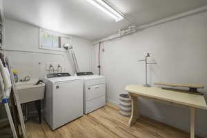 Laundry area with washer and dryer, light wood-type flooring, and a sink