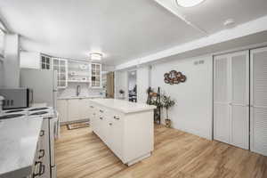 Kitchen with stainless steel microwave, a sink, white range with electric cooktop, light wood-style flooring, and white cabinetry
