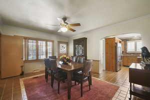 Dining room featuring arched walkways, light tile patterned floors, ornamental molding, ceiling fan, and baseboards