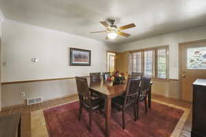 Tiled dining space with ceiling fan and crown molding