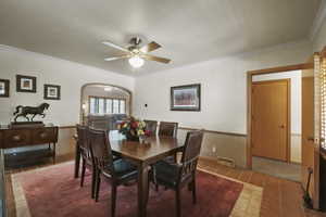 Tiled dining space with arched walkways, crown molding, and ceiling fan