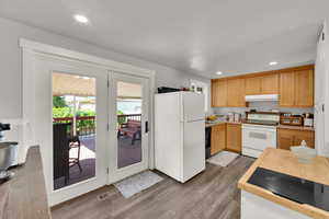 Kitchen with white appliances, under cabinet range hood, wood finished floors, light countertops, and recessed lighting