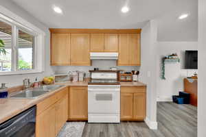 Kitchen featuring white electric range, under cabinet range hood, black dishwasher, a sink, and light wood-style floors