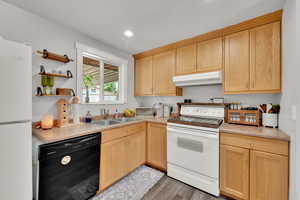 Kitchen with under cabinet range hood, white appliances, a sink, light wood-style flooring, and light brown cabinetry