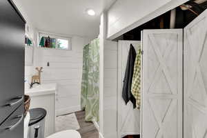 Bathroom with wood finished floors, vanity, toilet, a shower with curtain, and wooden walls