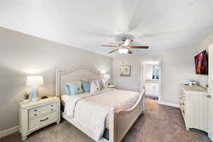 Bedroom with dark carpet, baseboards, ceiling fan, and ensuite bathroom