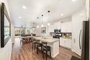 Kitchen with stainless steel appliances, wood finished floors, decorative backsplash, white cabinets, and recessed lighting