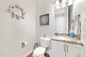 Half bath with toilet, vanity, wood finished floors, and baseboards