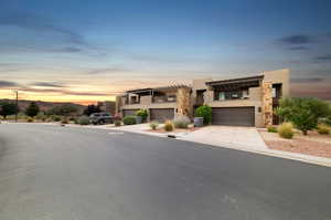 View of front of house with a garage, stucco siding, concrete driveway, stone siding, and a balcony