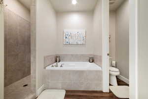 Bathroom featuring toilet, a garden tub, wood finished floors, and tiled shower