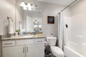 Full bathroom with vanity, toilet, shower / bath combo with shower curtain, and ceiling fan