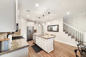 Kitchen featuring stainless steel appliances, a sink, light wood-type flooring, backsplash, and white cabinetry