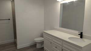 Full bath with toilet, wood finished floors, vanity, and baseboards